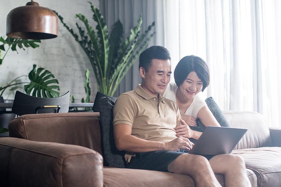 Insurance Quote - Married Couple Use a Laptop in Their Living Room on a Leather Sofa With Plants and Bright Light Around Them